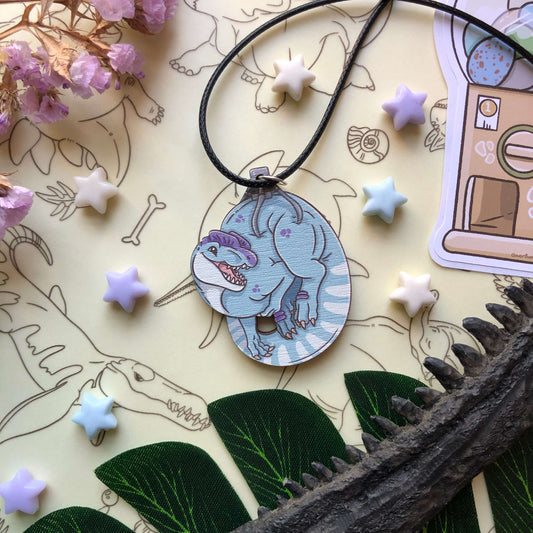 A blue and purple Dilophosaurus necklace. The Dilophosaurus is being held by a claw machine claw!