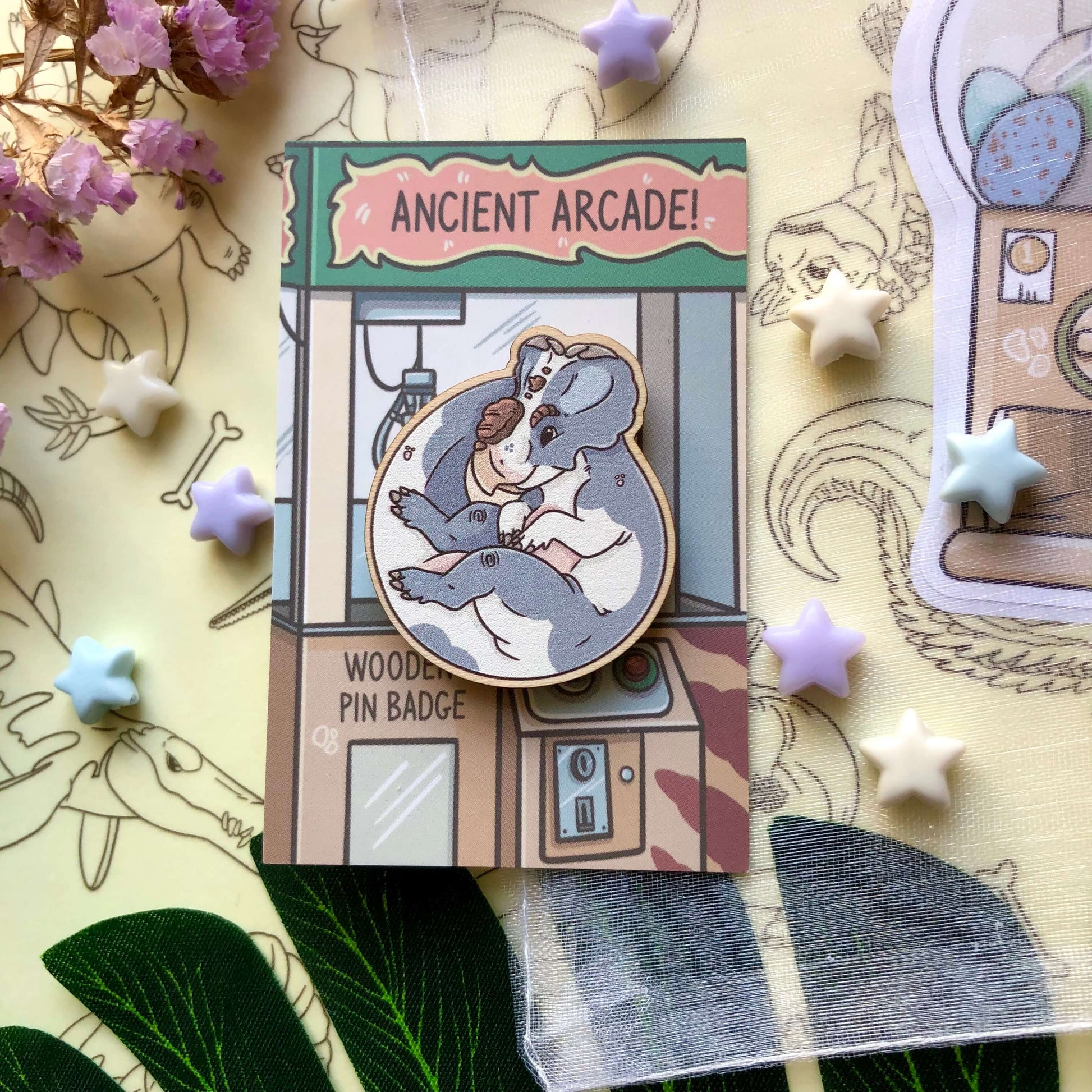 A wooden pin badge of a blue and white cow print Pachyrhinosaurus! It is on a backing card designed to look like a claw machine.