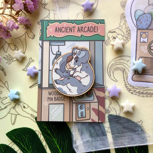 A wooden pin badge of a blue and white cow print Pachyrhinosaurus! It is on a backing card designed to look like a claw machine.