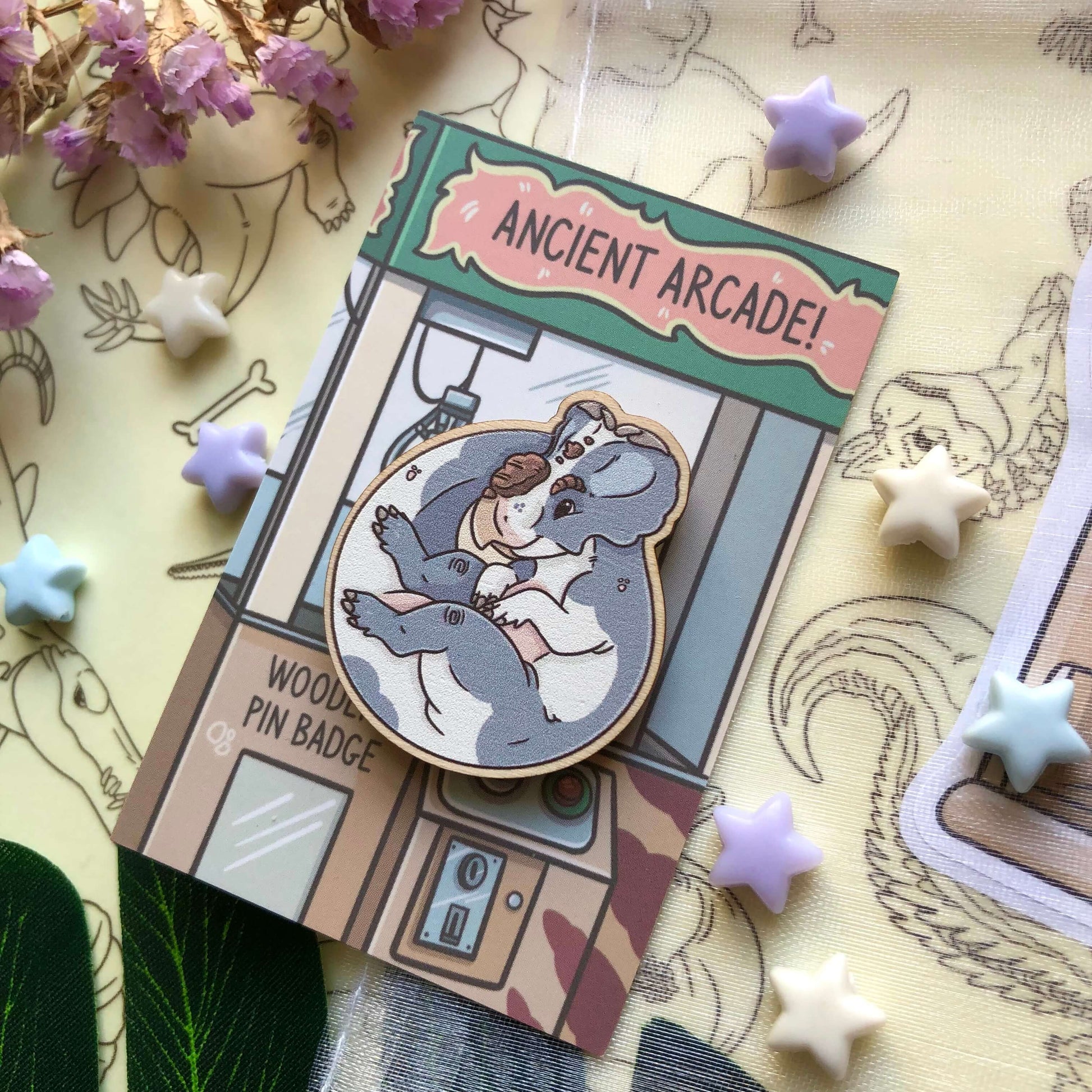 A wooden pin badge of a blue and white cow print Pachyrhinosaurus! It is on a backing card designed to look like a claw machine.