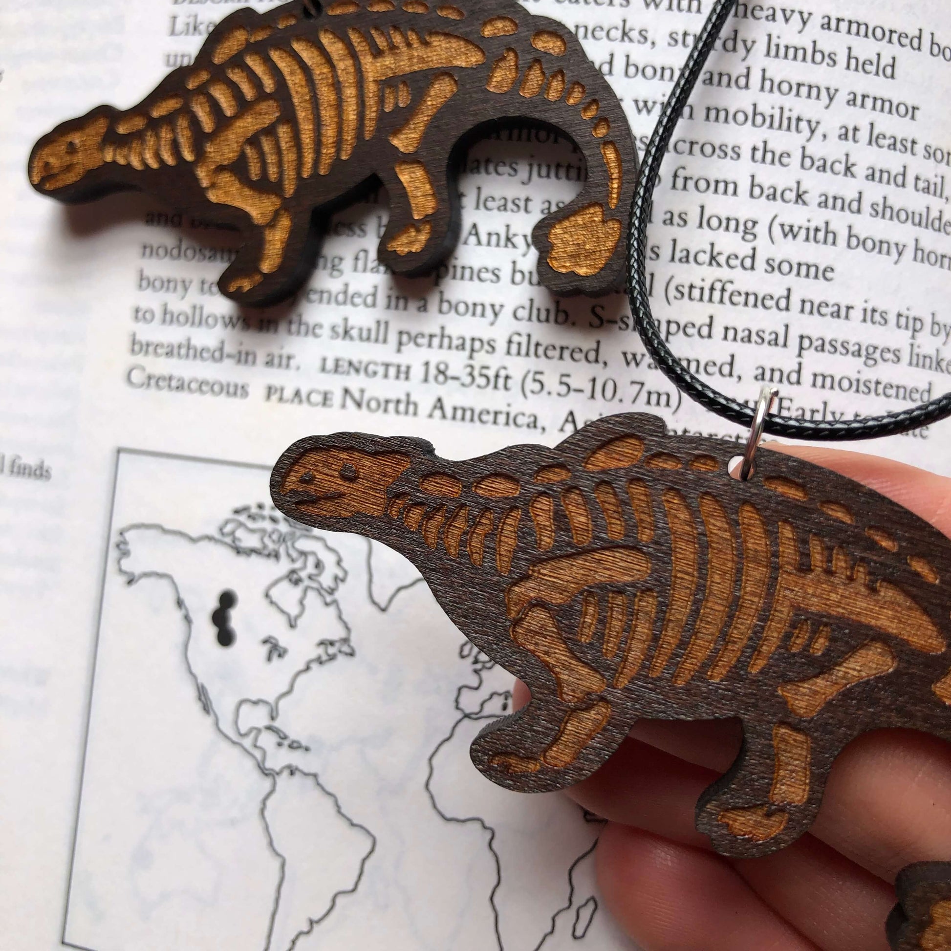 A pair of wooden necklaces of stylised Ankylosaurus skeletons. The skeleton is engraved and one is painted metallic gold.