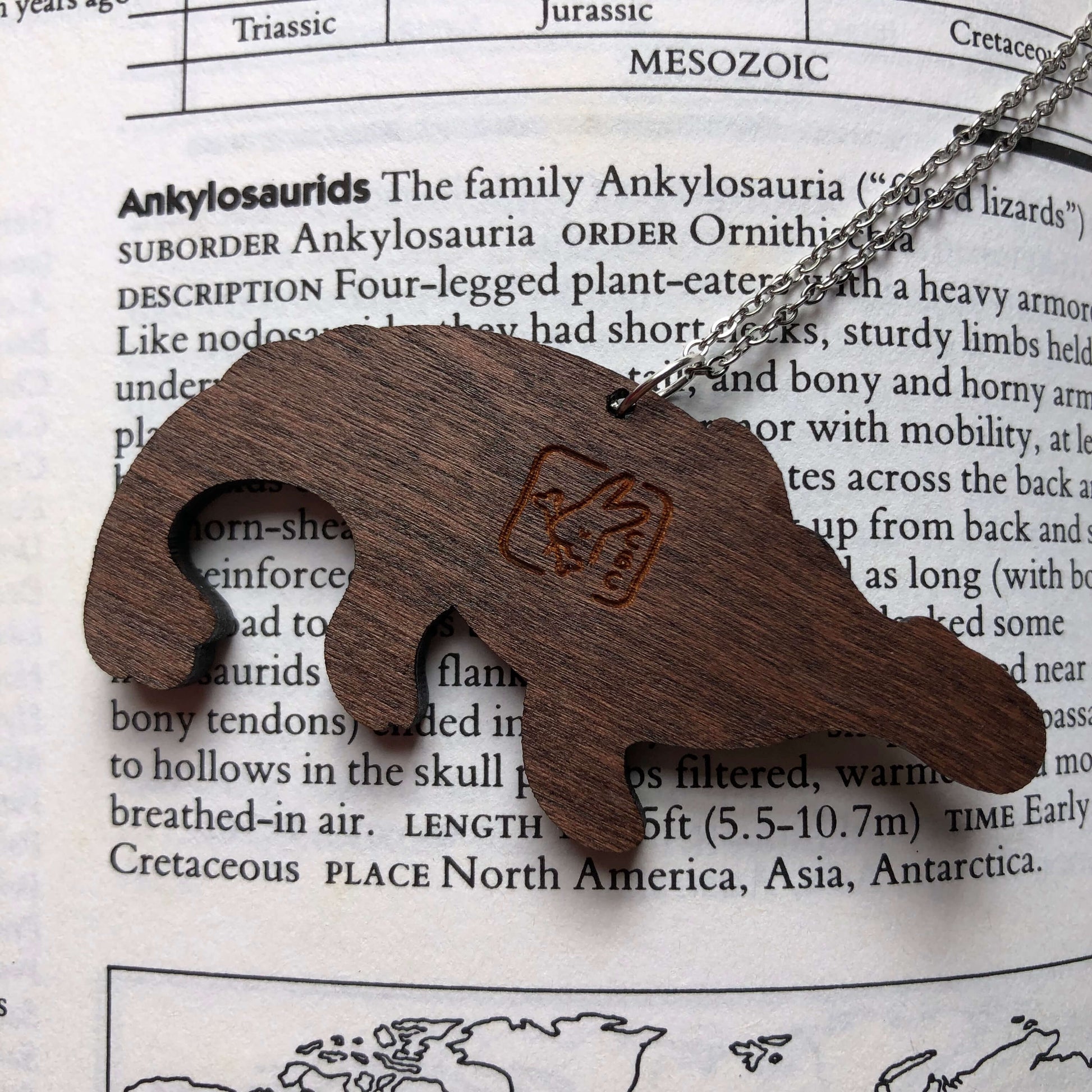 The back of a wooden necklace of a stylised Ankylosaurus skeleton. The Clever Bunny Logo is engraved into the wood. It is hanging on a stainless steel chain.