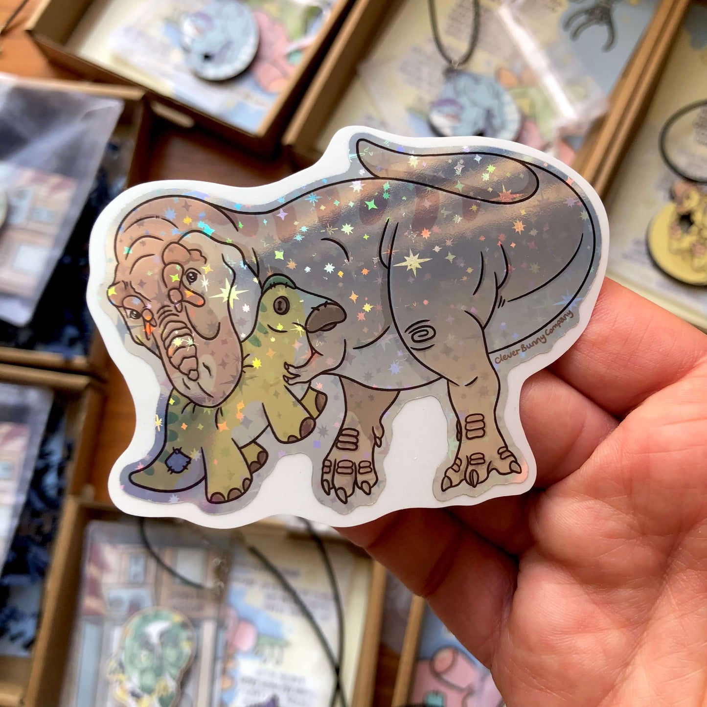 A holographic sticker of a Tyrannosaurus rex holding a plush toy of an Edmontosaurus in its mouth!
