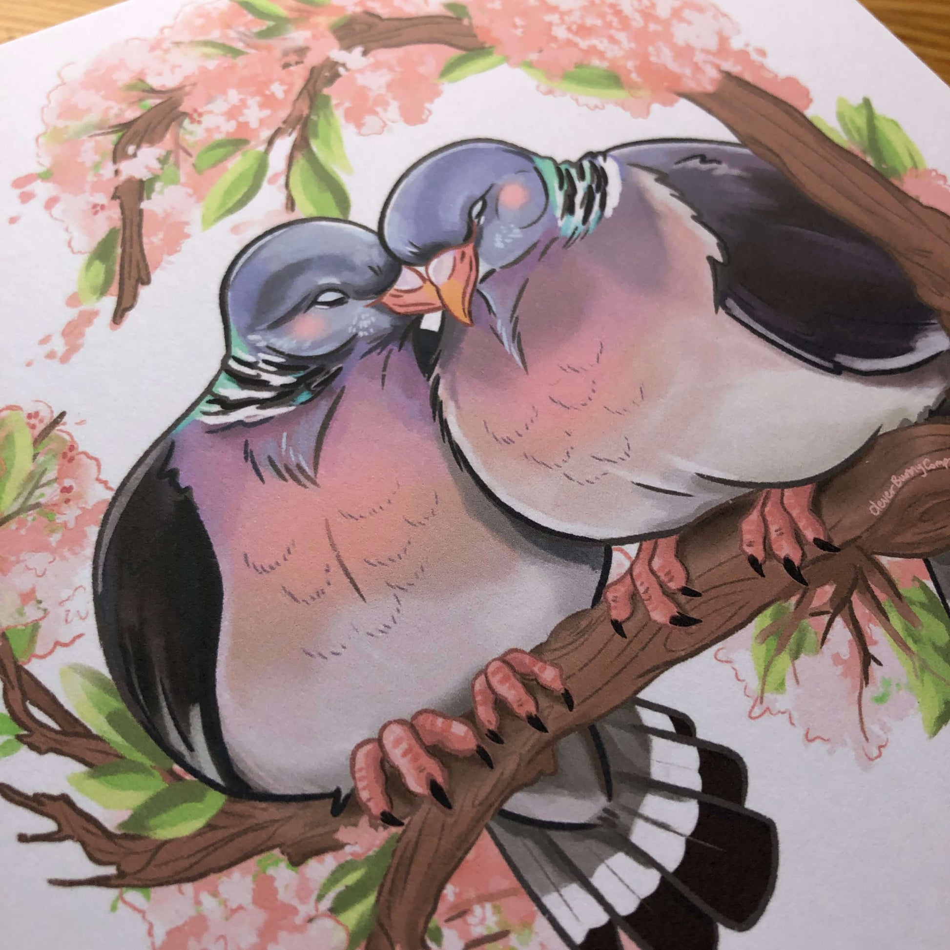 A square art print of an illustration of two woodpigeons with their heads touching. The pigeons are perched on a branch of cherry blossom.