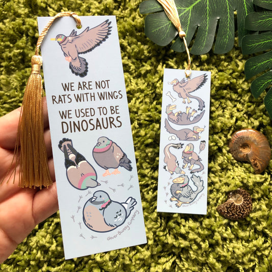 A pigeon themed bookmark, text reads "We are not rats with wings, we used to be dinosaurs". Reverse of the bookmark shows pigeon-coloured raptors. The bookmark has a gold tassel.