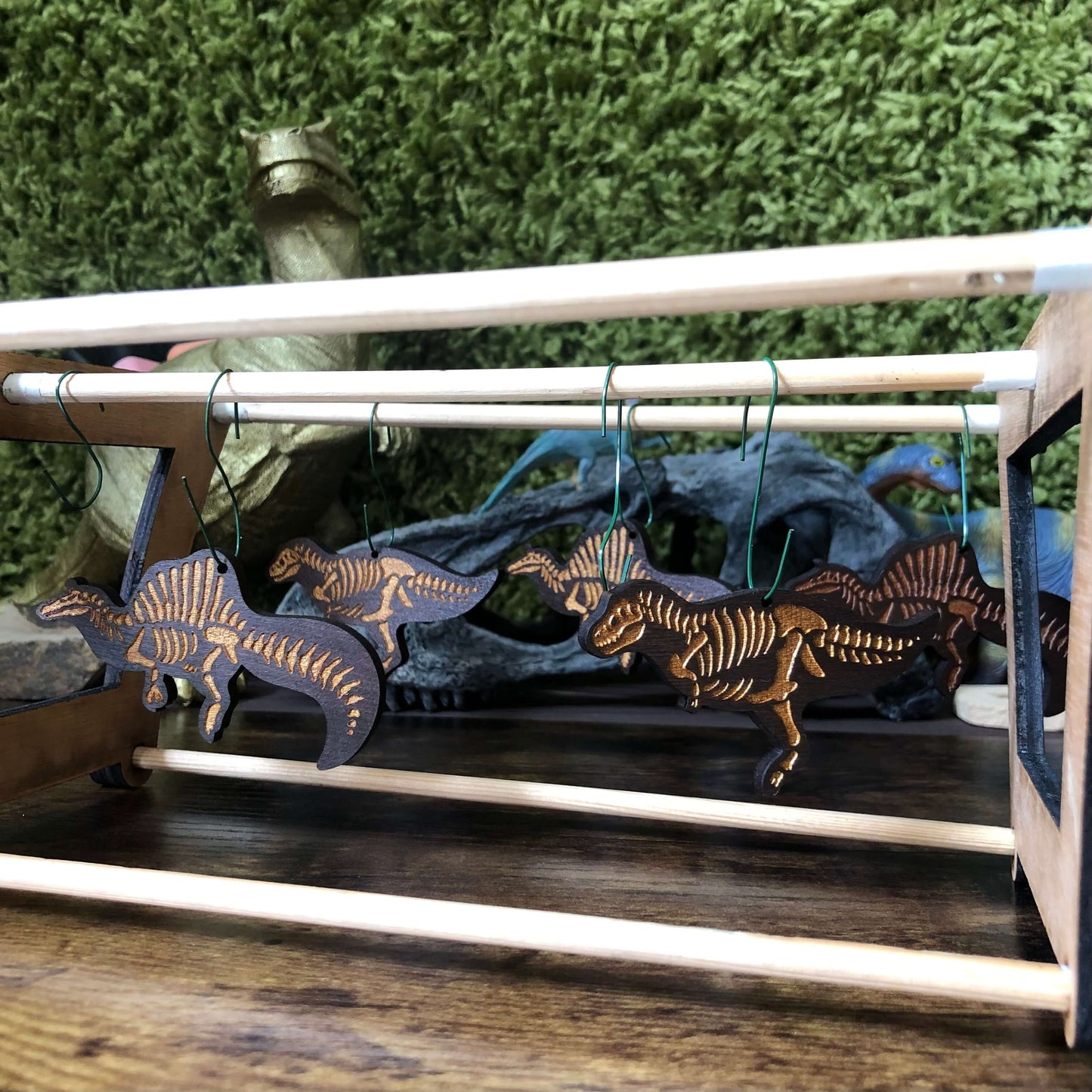 Wooden dinosaur skeleton necklaces hanging on a rack with a mossy background