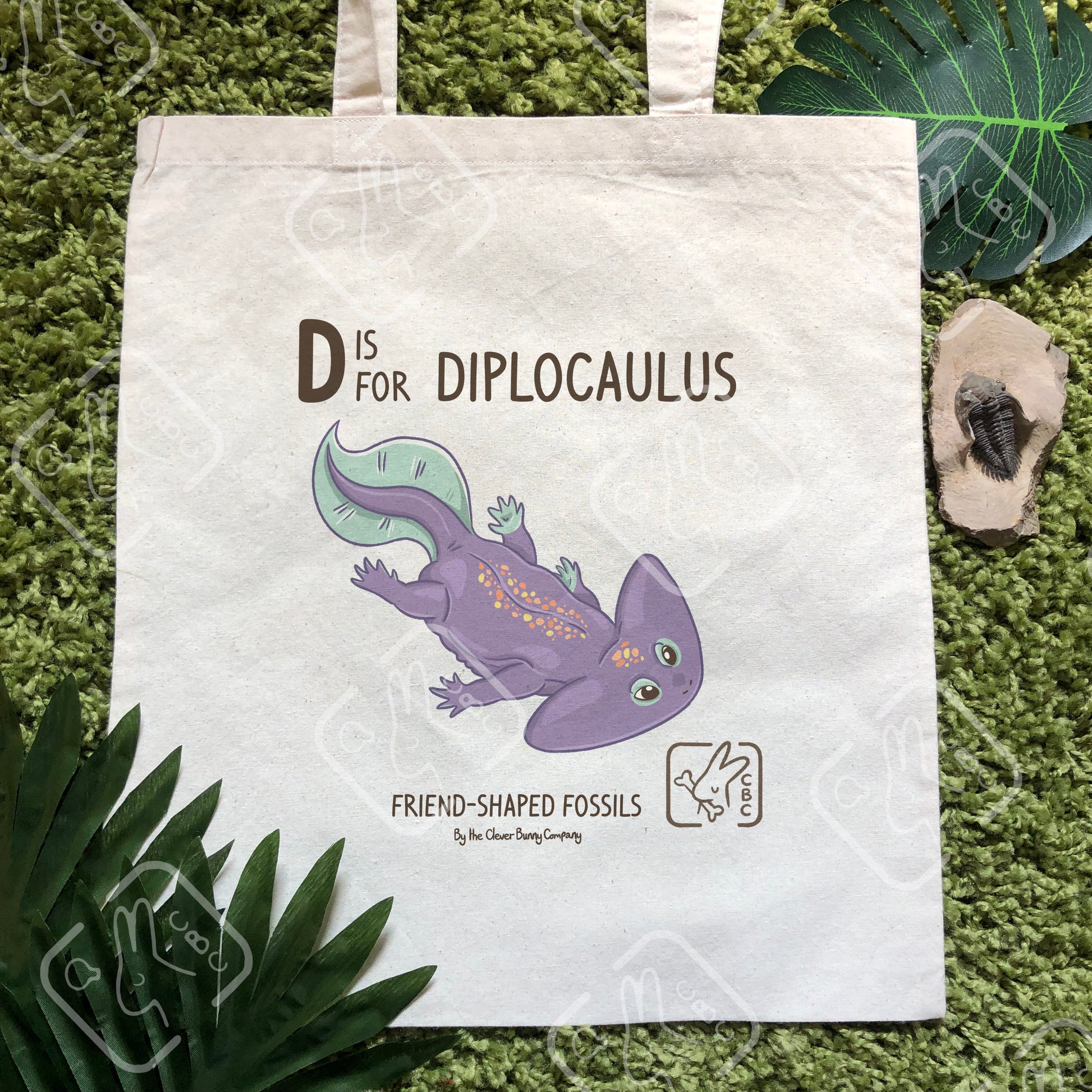 A tote bag featuring a purple Diplocaulus. Text reads "D is for Diplocaulus" and "Friend-shaped Fossils by the Clever Bunny Company."