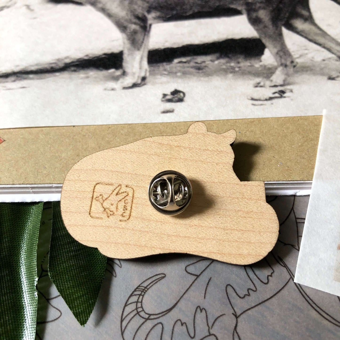 Back of a wooden engraved pin badge of a Thylacine holding a sign that reads “shy”. Shows a silver metal pin and the Clever Bunny Company logo engraved on the back.